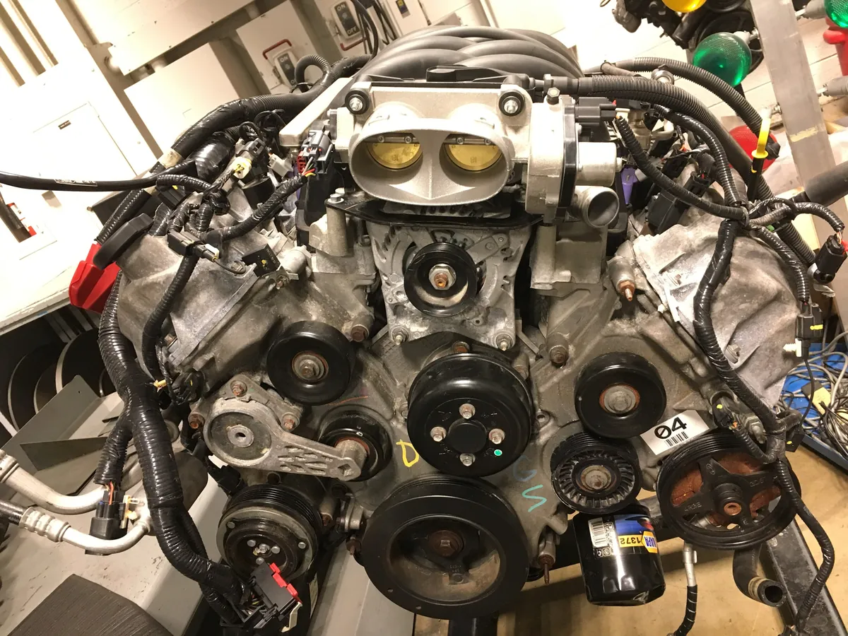 A Ford V8 engine with its belts, pulleys and wiring, in a repair shop