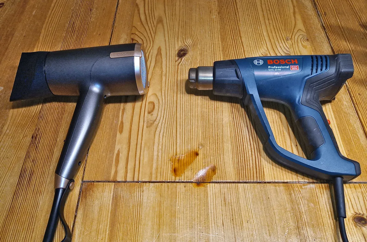 A hair dryer and a heat gun lying side by side on a wooden floor