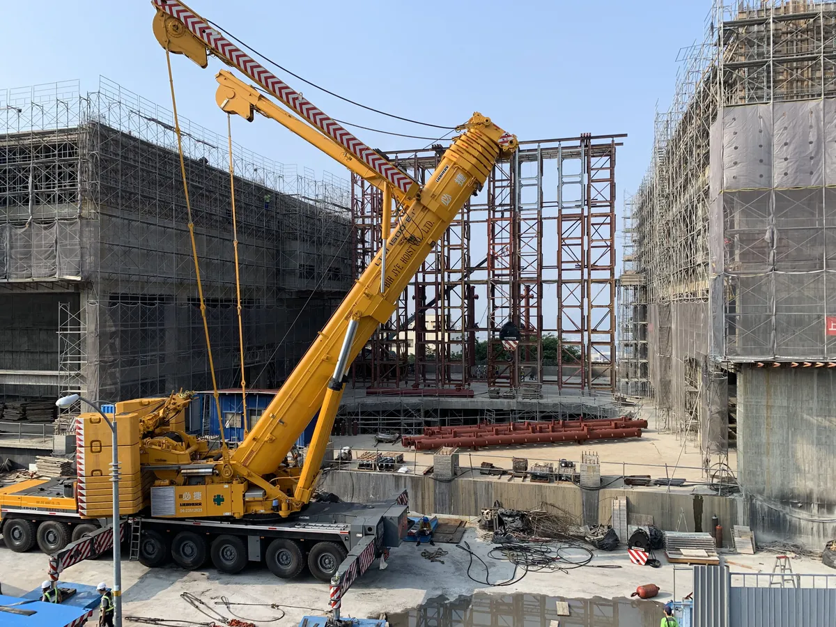A yellow Liebherr all-terrain crane lifting next to a building under construction