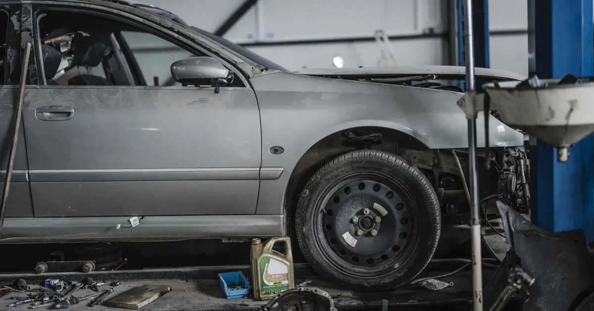 A grey car up on a lift in a repair shop, with parts taken off and tools on the floor