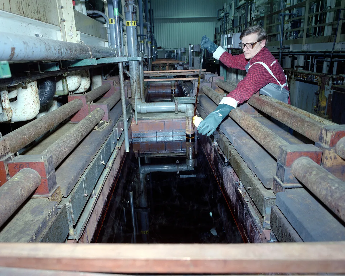 A worker taking a sample from a chrome plating tank