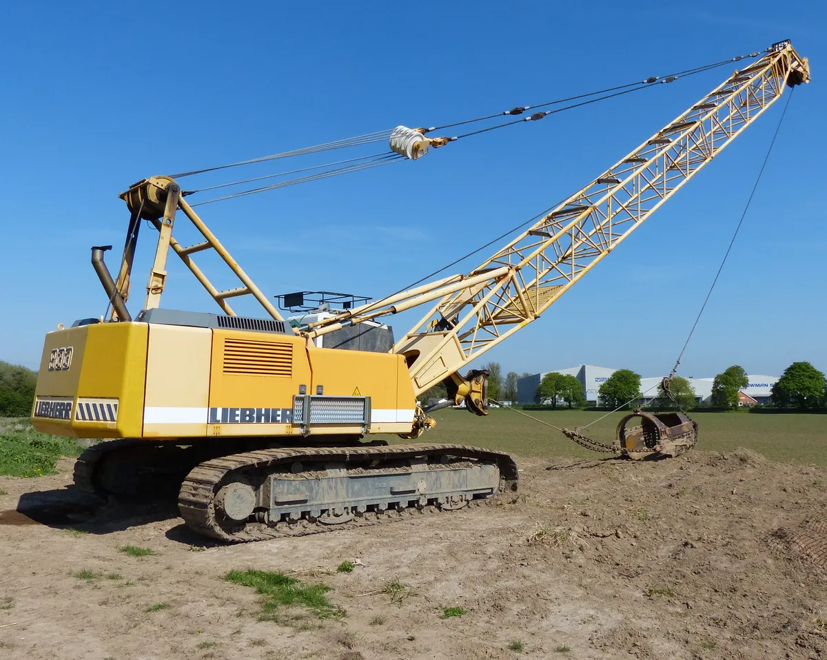 A yellow Liebherr crawler crane with a long lattice boom on open ground