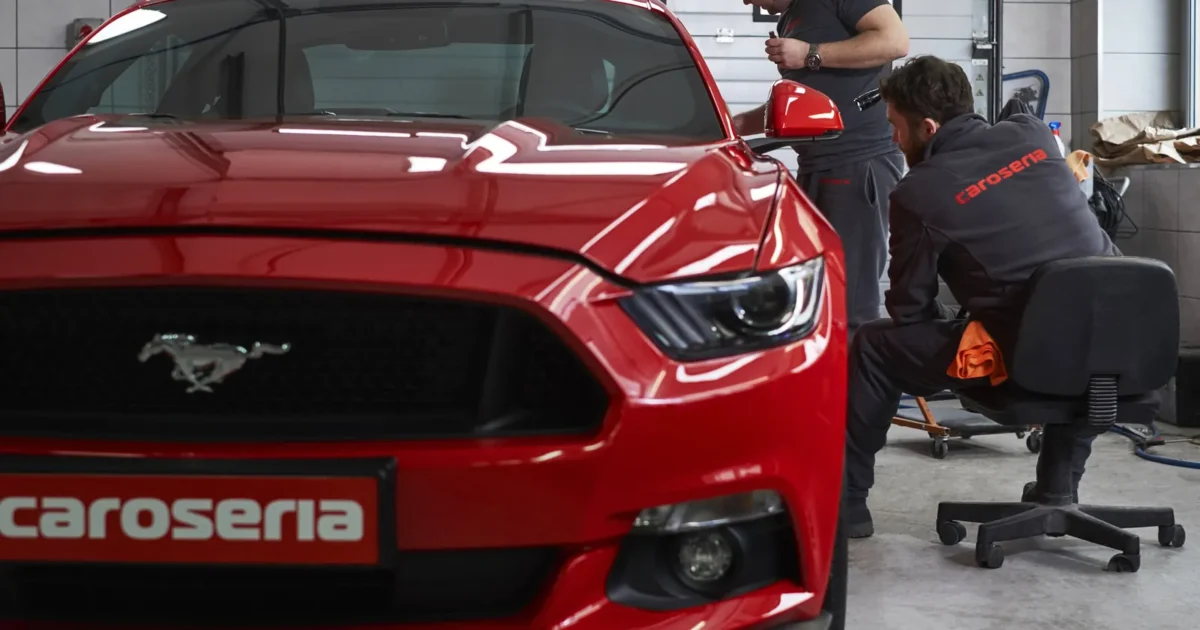 Two detailers working on the paint of a red Ford Mustang in a detailing shop
