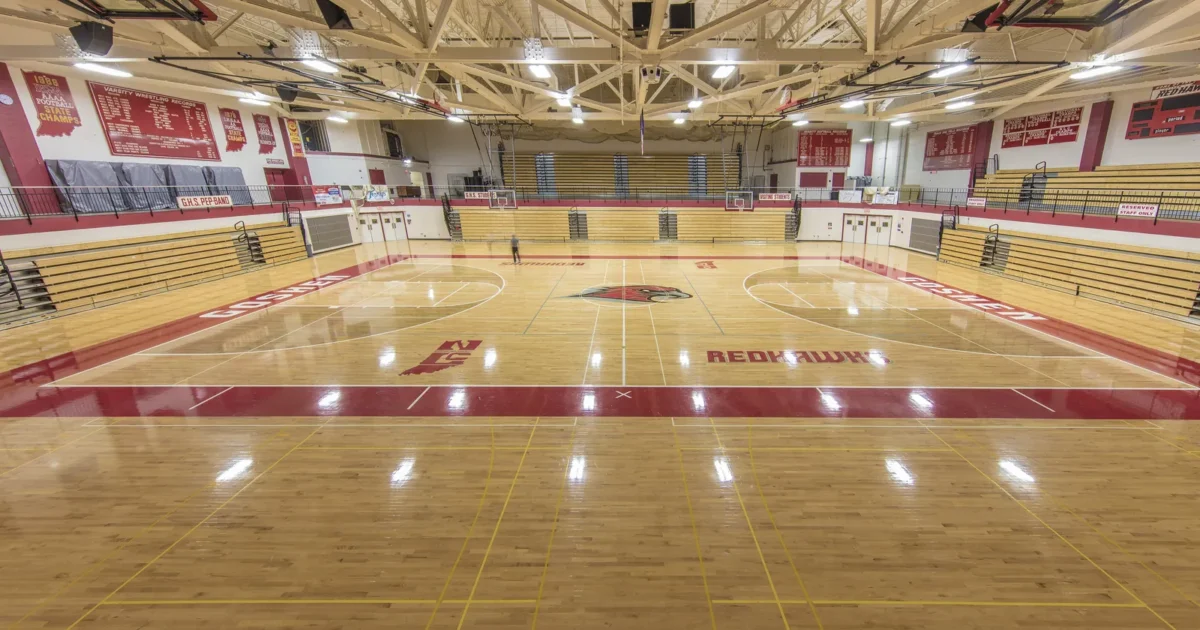 An empty high school gym with a wooden basketball court and bleachers