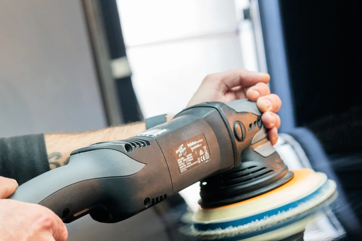A detailer using a machine polisher on a car's dark paint