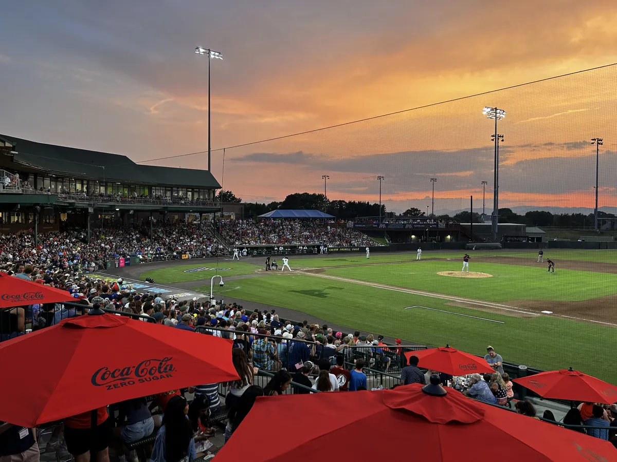 Fans under red umbrellas watching a minor league baseball game at sunset