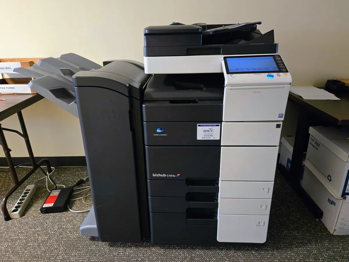 A large office photocopier with a paper finisher on its side