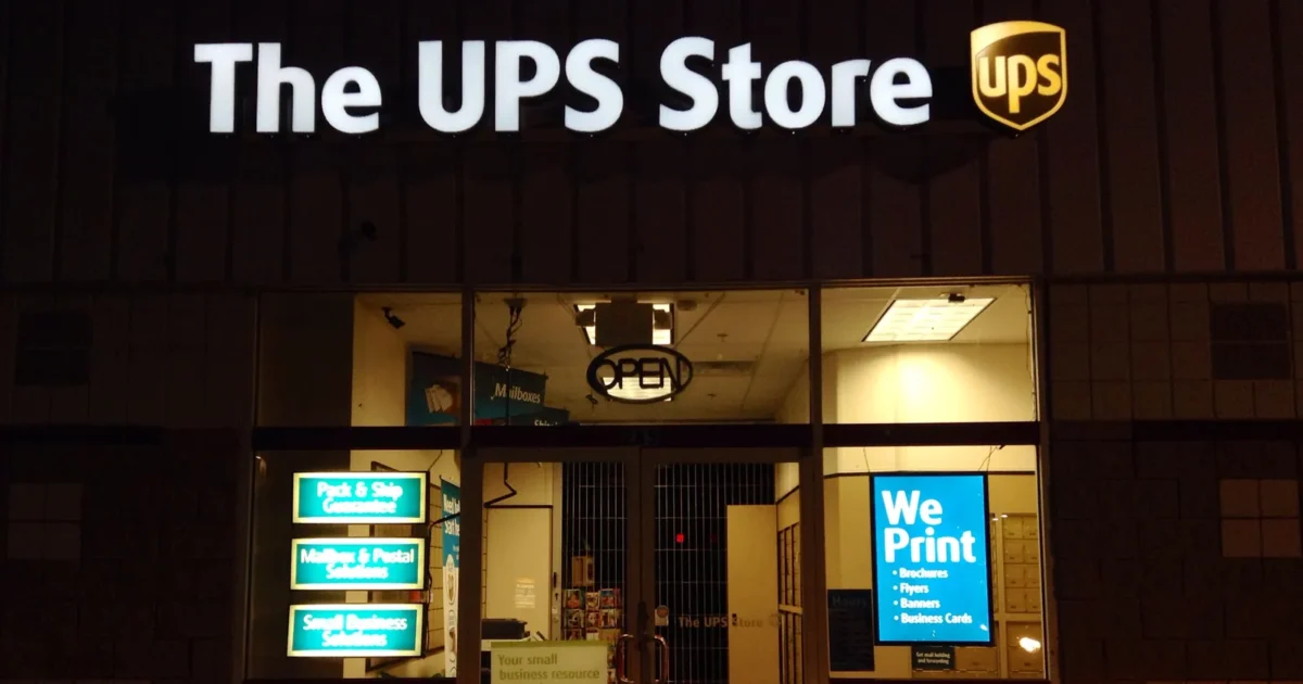 The front of a UPS Store at night, with a We Print sign in the window