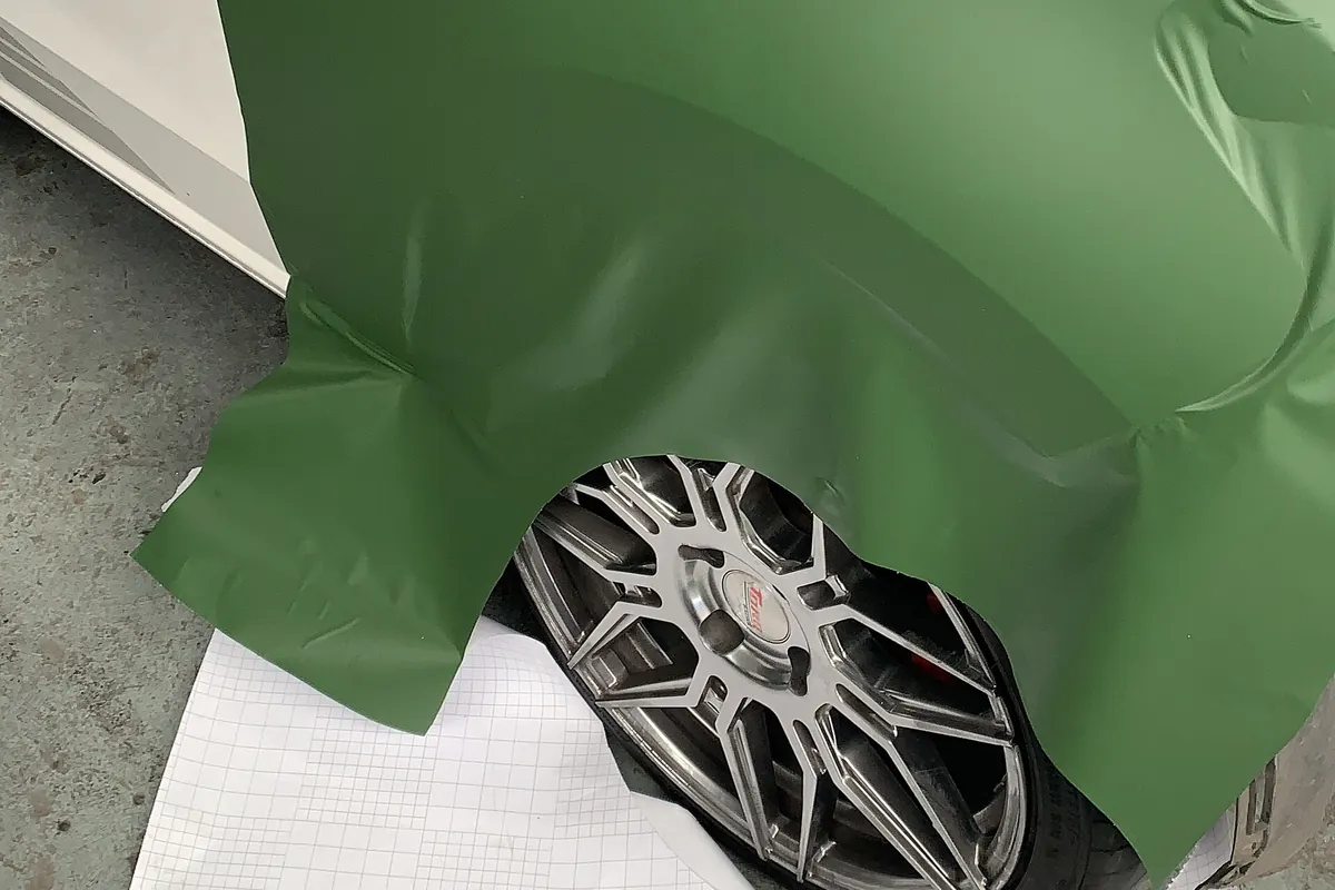 Green vinyl wrap film being stretched over a car's front wheel arch