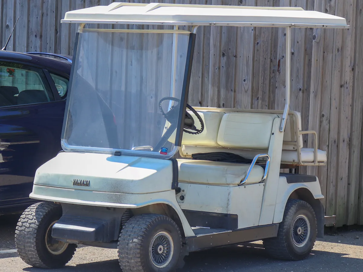 A white Yamaha golf cart with a roof parked on grass