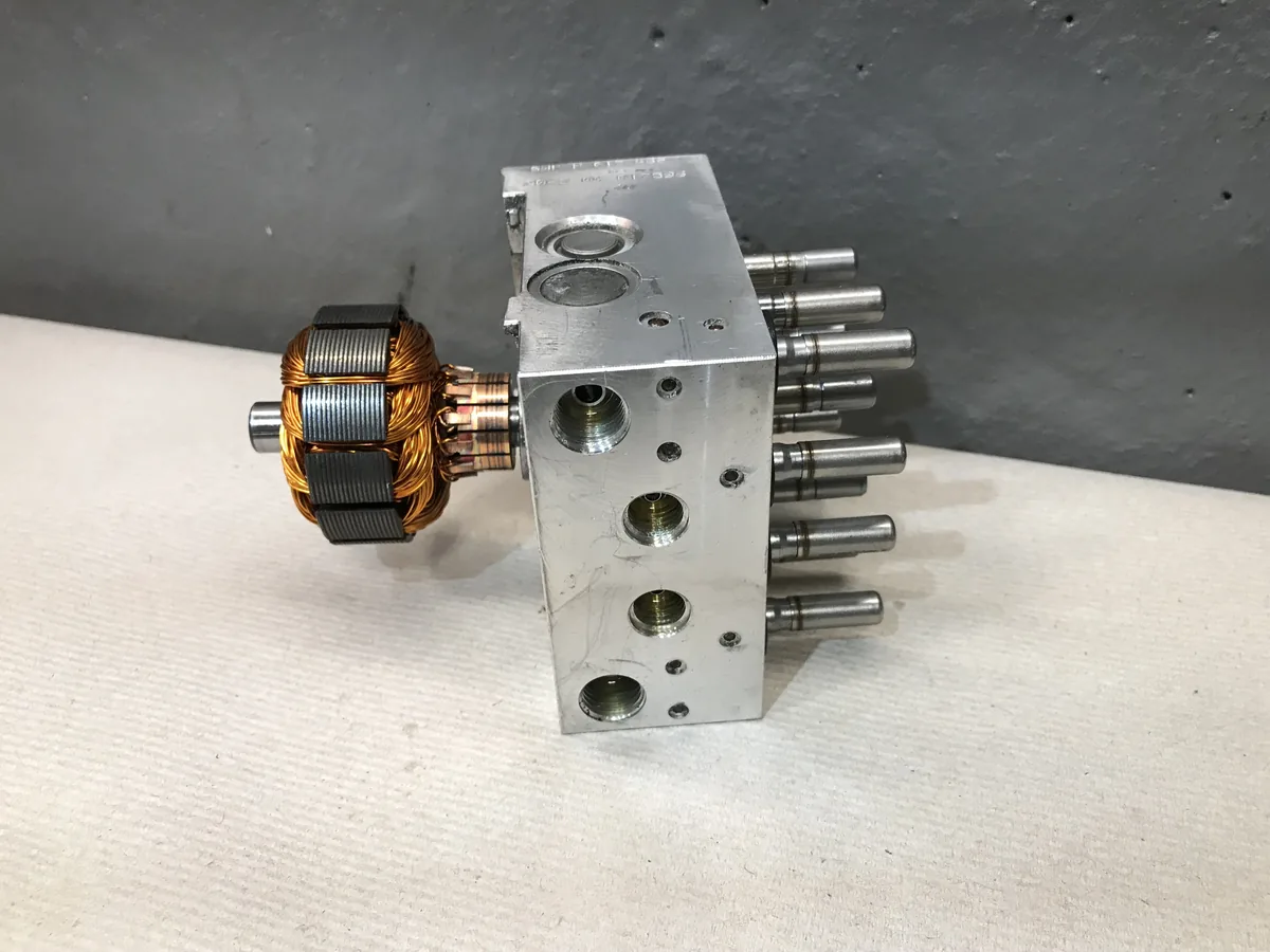 An ABS hydraulic control unit off the car: an aluminum valve block with valve stems on top and a copper motor winding on the side