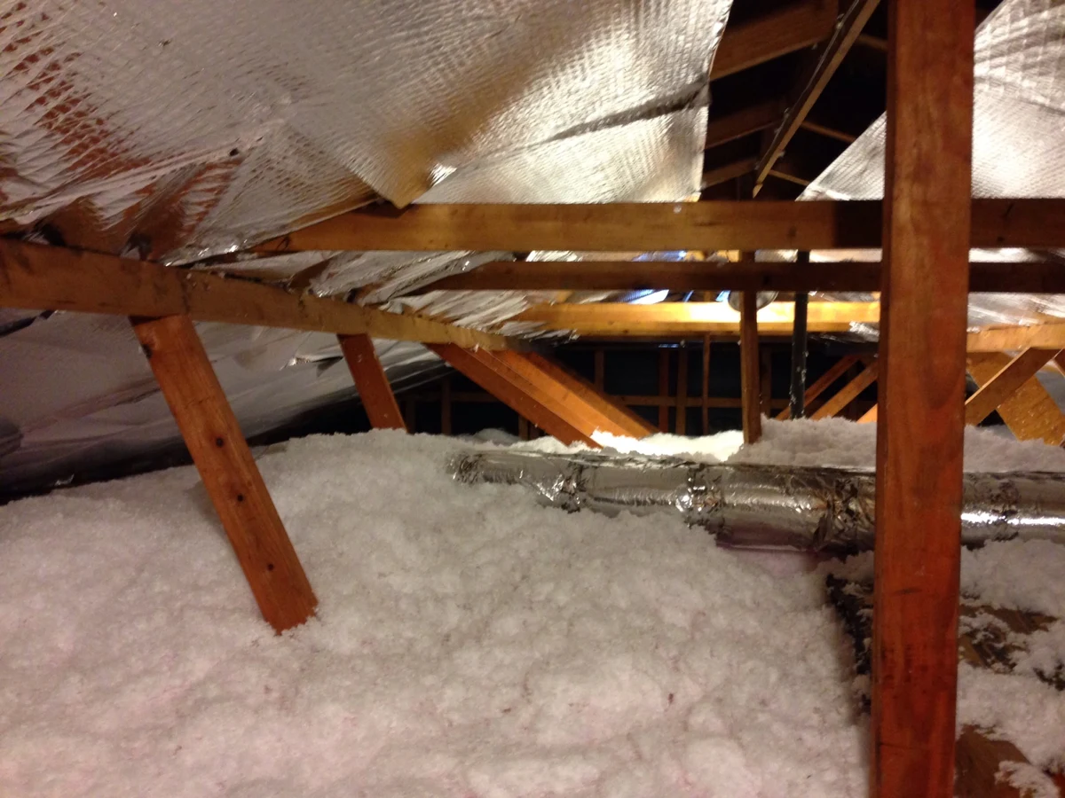 Loose insulation spread across an attic floor beneath exposed roof framing.