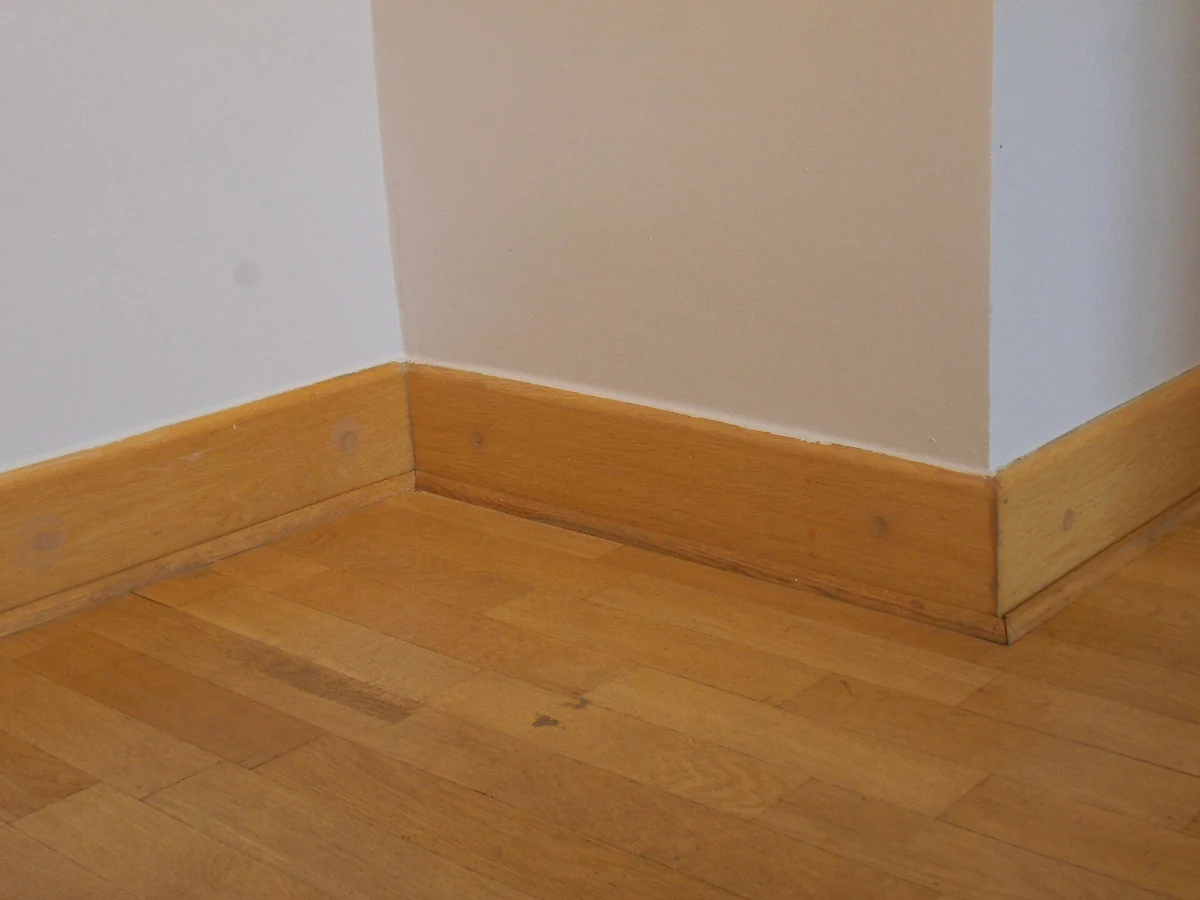 Wood baseboard fitted into an inside corner at the edge of a wood floor.