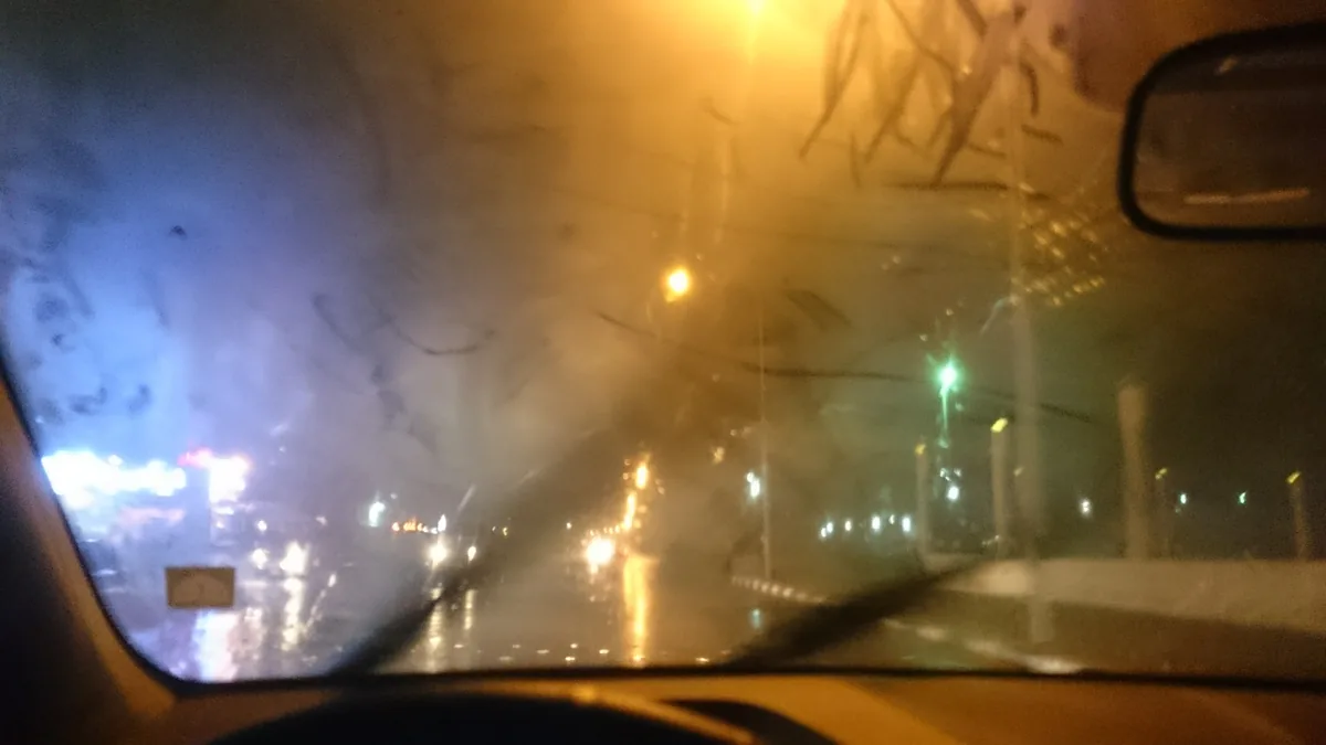 The inside of a car windshield fogged over at night, with street lights blurred through it