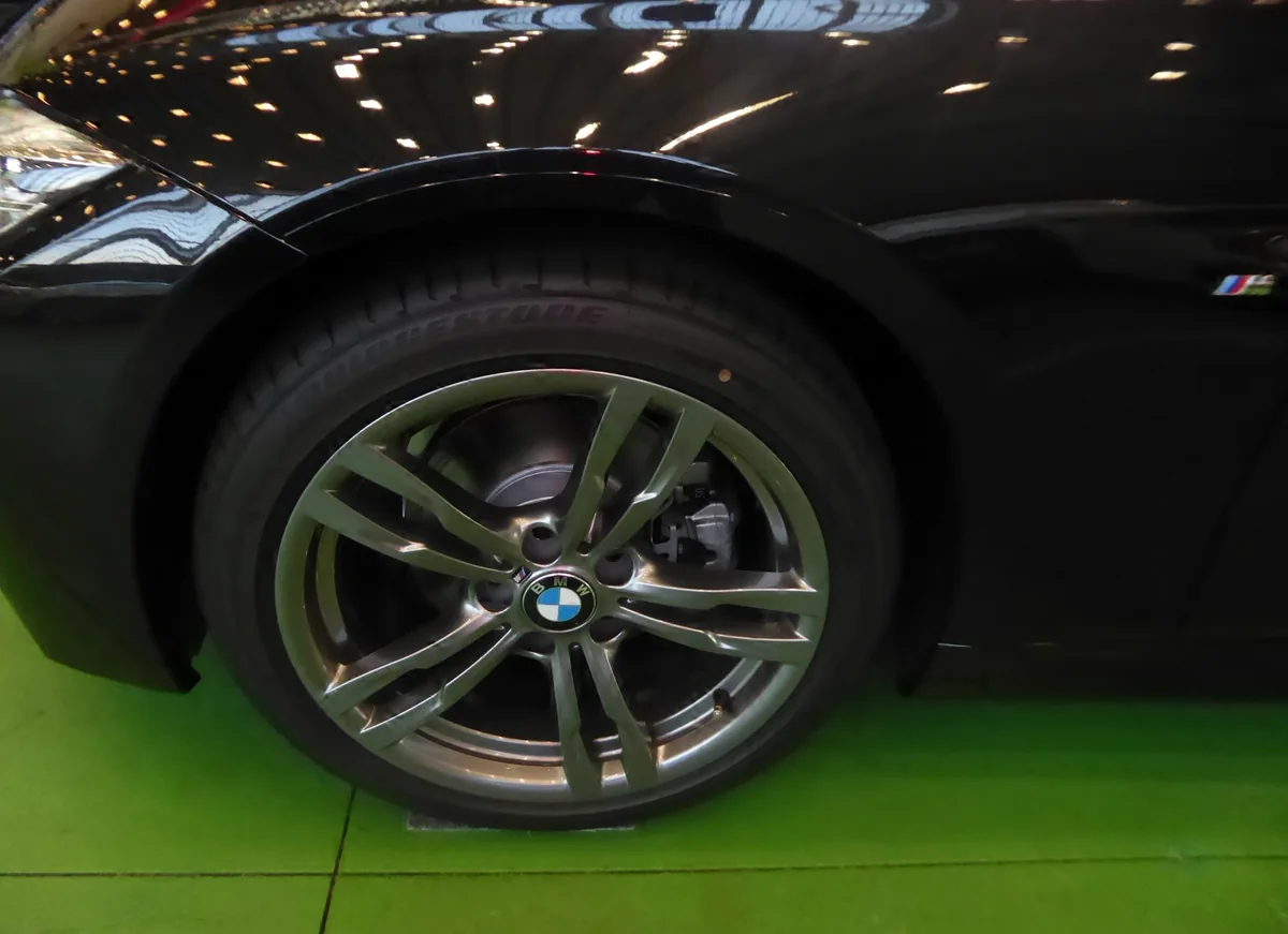 The front wheel of a BMW 320d M Sport, with the brake rotor visible behind the spokes.