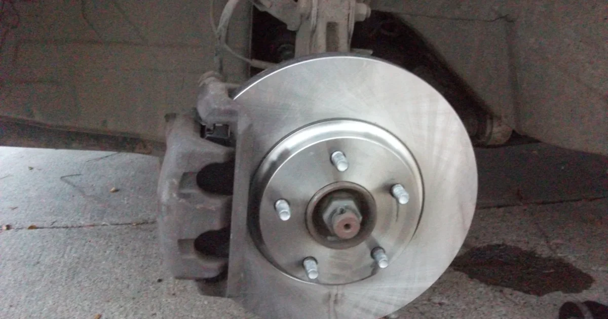 The front brake of a car with the wheel off, showing a shiny brake disc and the caliper behind it