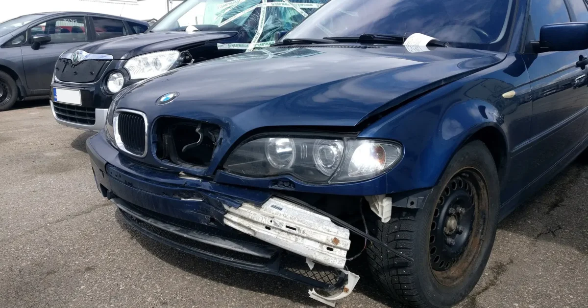 A dark blue sedan in a parking lot with its front bumper cover cracked and hanging loose on one side