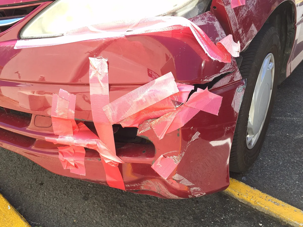 A red car whose torn front bumper is held together with strips of duct tape