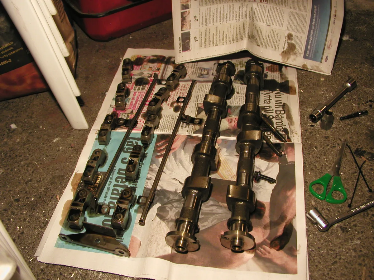 Two camshafts and the small valve parts of an engine laid out on newspaper on a garage floor