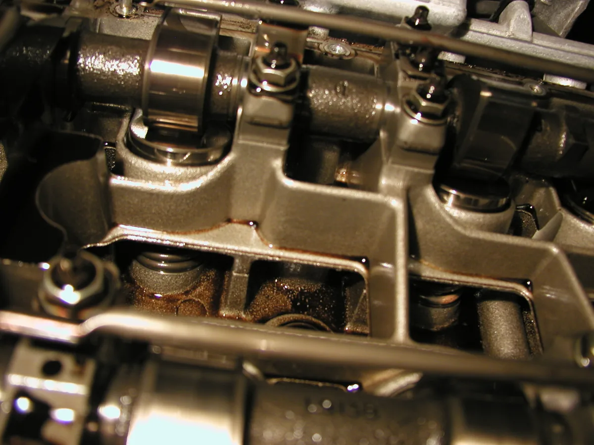 Close up inside an open cylinder head: a camshaft lobe resting on a round valve lifter