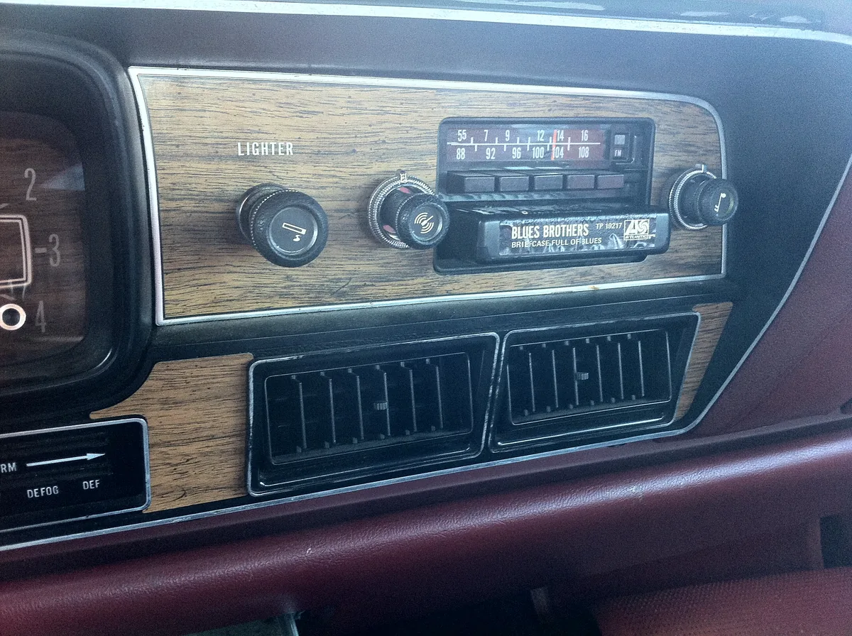 The center of an older car dashboard with a radio above two wide black air vents