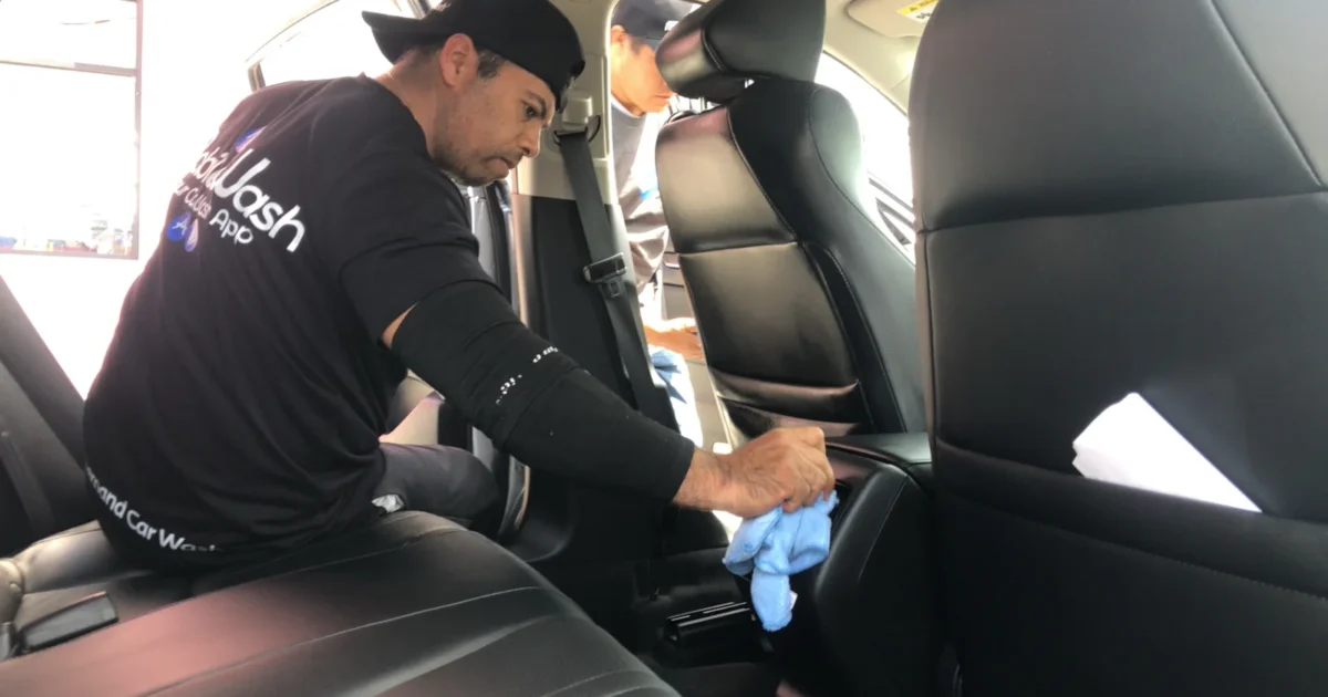 A detailer wiping an interior surface beside a car seat.