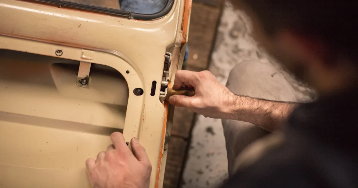 Hands working on the lock at the edge of a car door with its interior trim removed.
