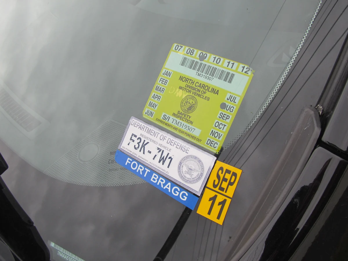 An older North Carolina safety inspection sticker beside a Department of Defense vehicle pass.
