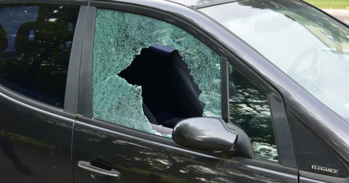 A black car with shattered front door glass and a large hole in the pane.