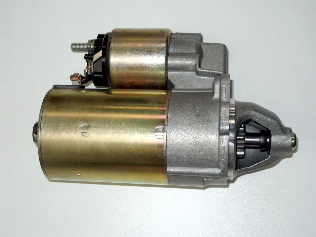 A car starter motor on a white background: the round motor body, the solenoid on top and the small gear at the front