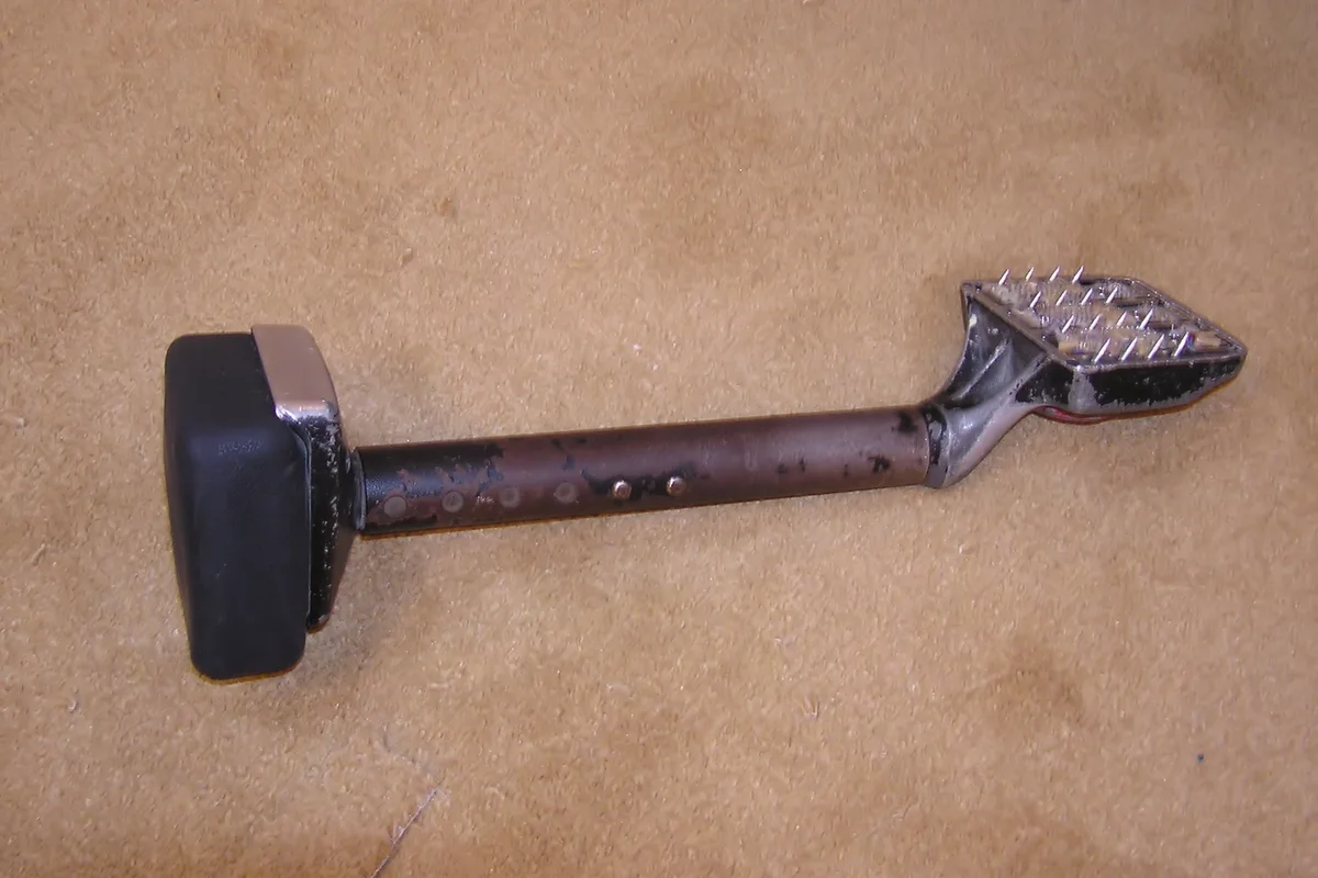 A knee kicker with a padded end and toothed carpet-gripping head resting on carpet.