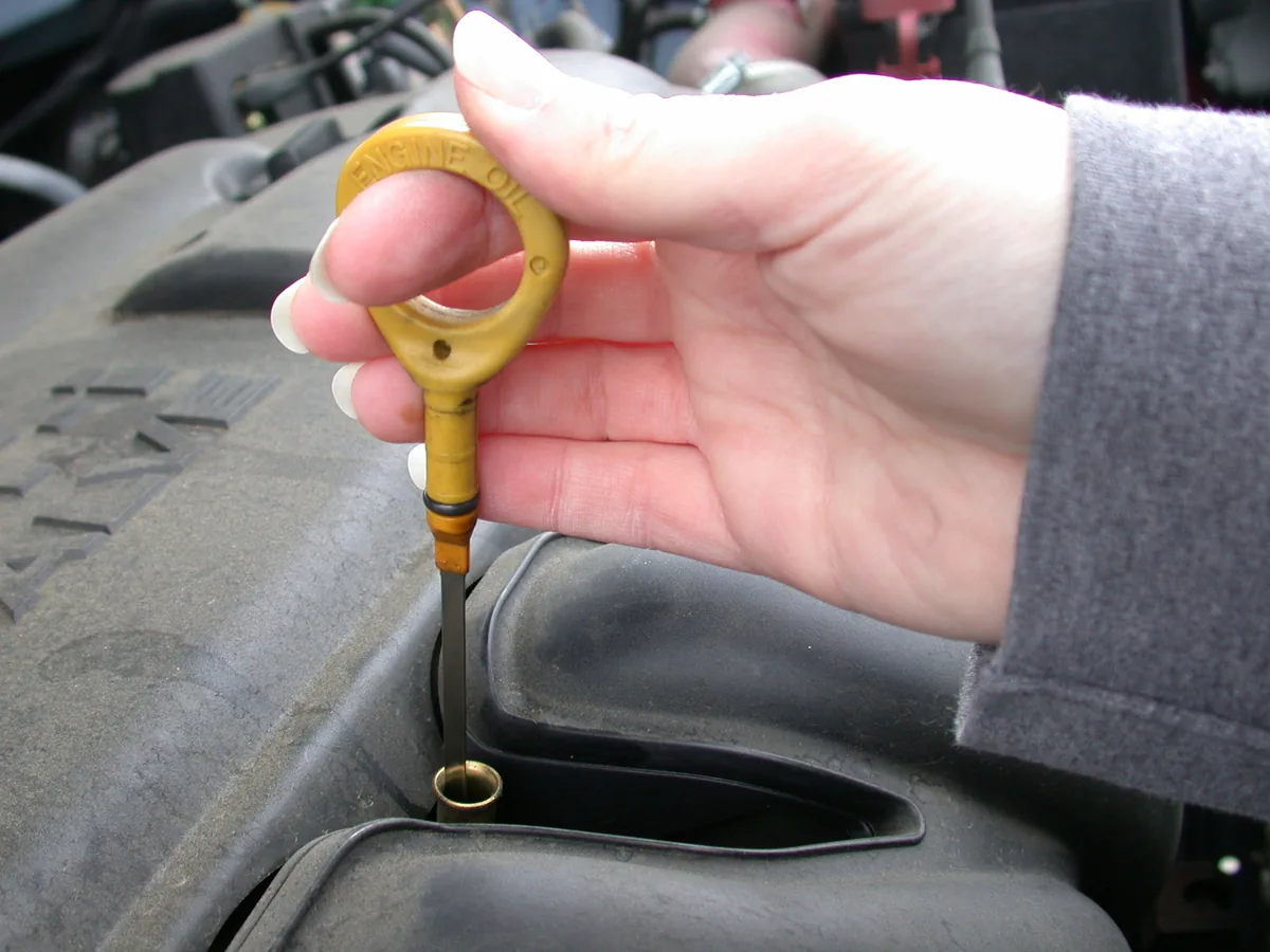 A hand pulling a yellow handled dipstick out of an engine