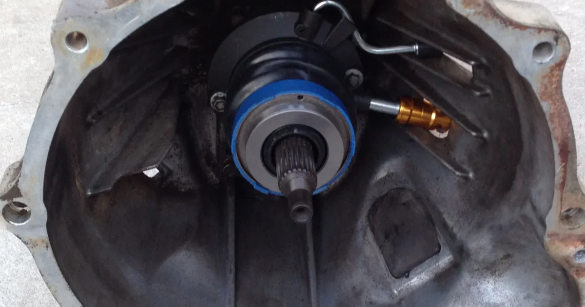 The inside of a manual gearbox bell housing, with a round slave cylinder and release bearing around the input shaft and a fluid line running to it