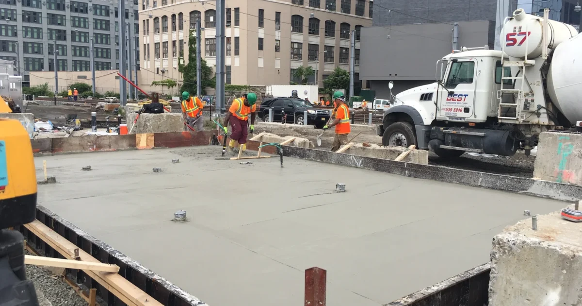 Workers finishing a newly poured concrete foundation at an MTA construction site.