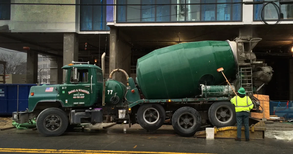 A green concrete mixer truck parked beside a construction site.