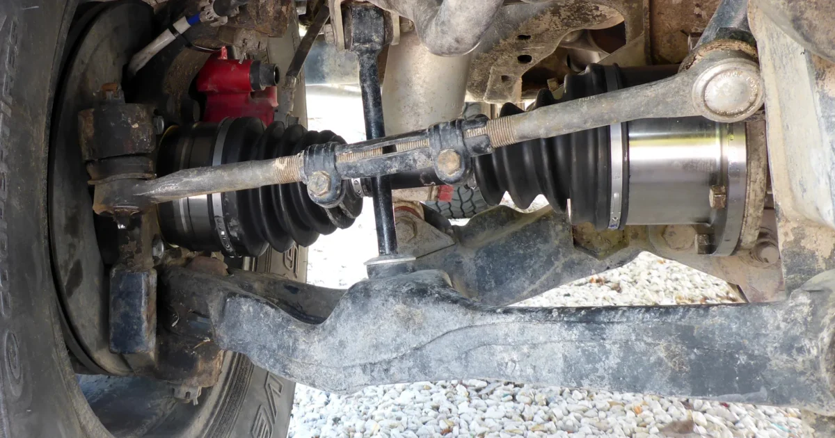 The underside of a truck front end with a new drive axle, its rubber boots and a long gray suspension arm