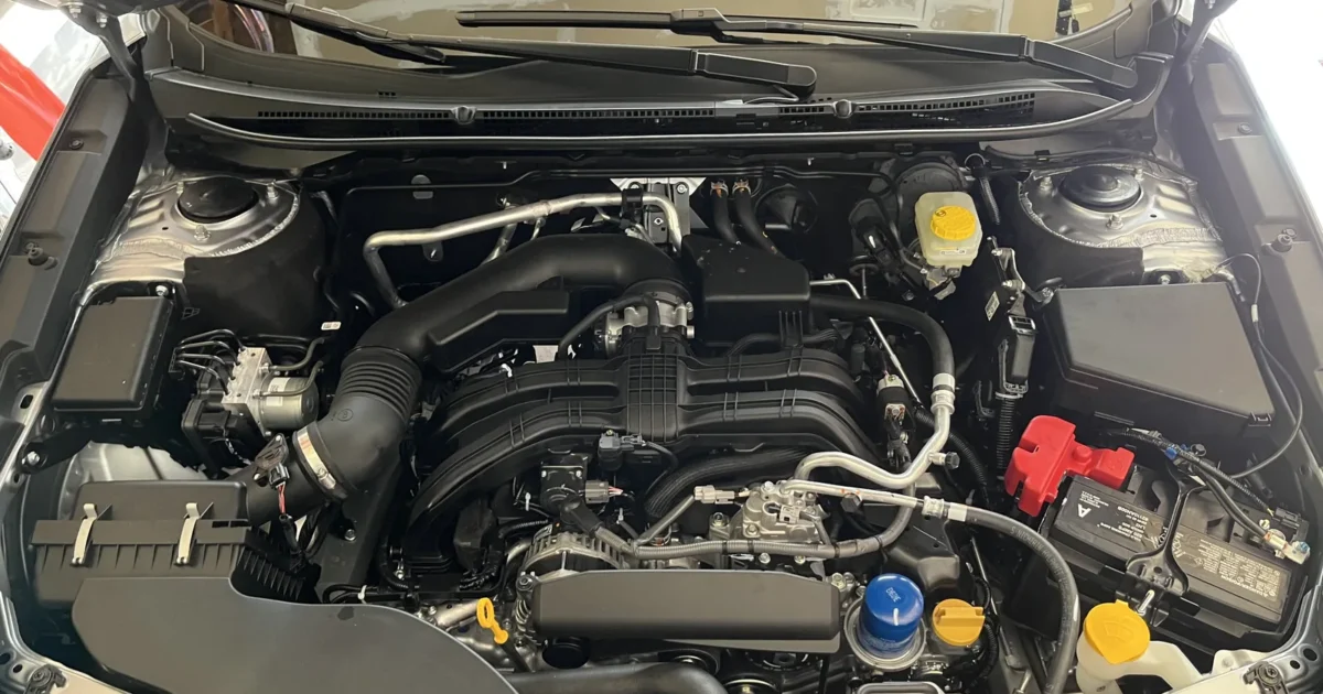 The open engine bay of a 2023 Subaru Outback, with the 2.5 liter engine, its hoses and the fluid caps