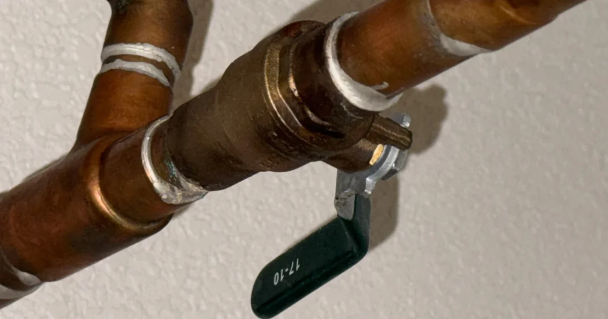 Real copper water supply pipes and a green-handled shutoff valve mounted near a wall.