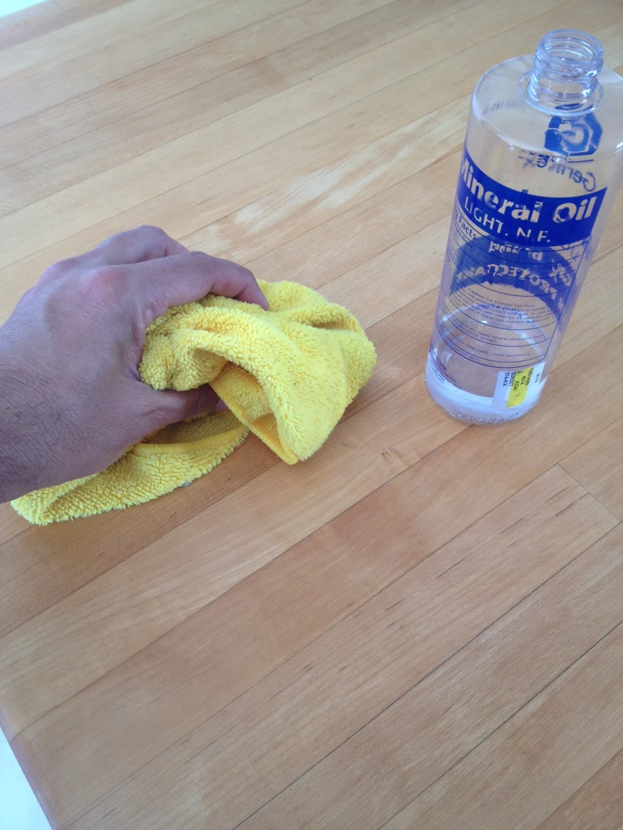A hand applies mineral oil to a butcher-block surface.