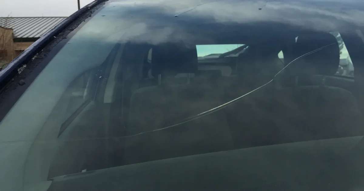 The windshield of a dark car with a long crack running across the glass