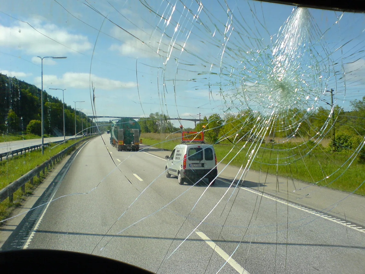 The view down a highway through a truck windshield covered in cracks spreading from one impact