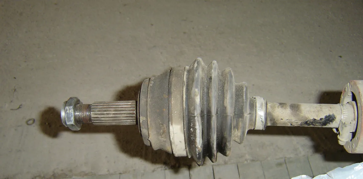 A front half axle lying on a floor, with its splined end, the ribbed rubber boot over the joint and the shaft