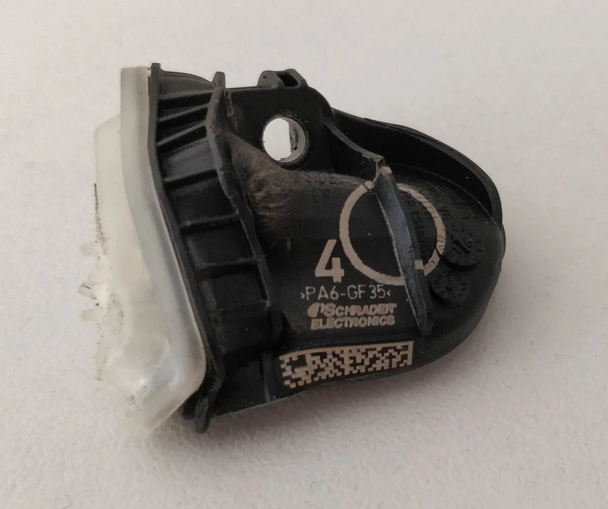 A removed black TPMS sensor with a damaged mounting area and no valve stem attached.
