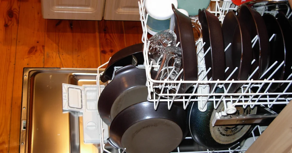An open dishwasher with plates and kitchen utensils in the rack.