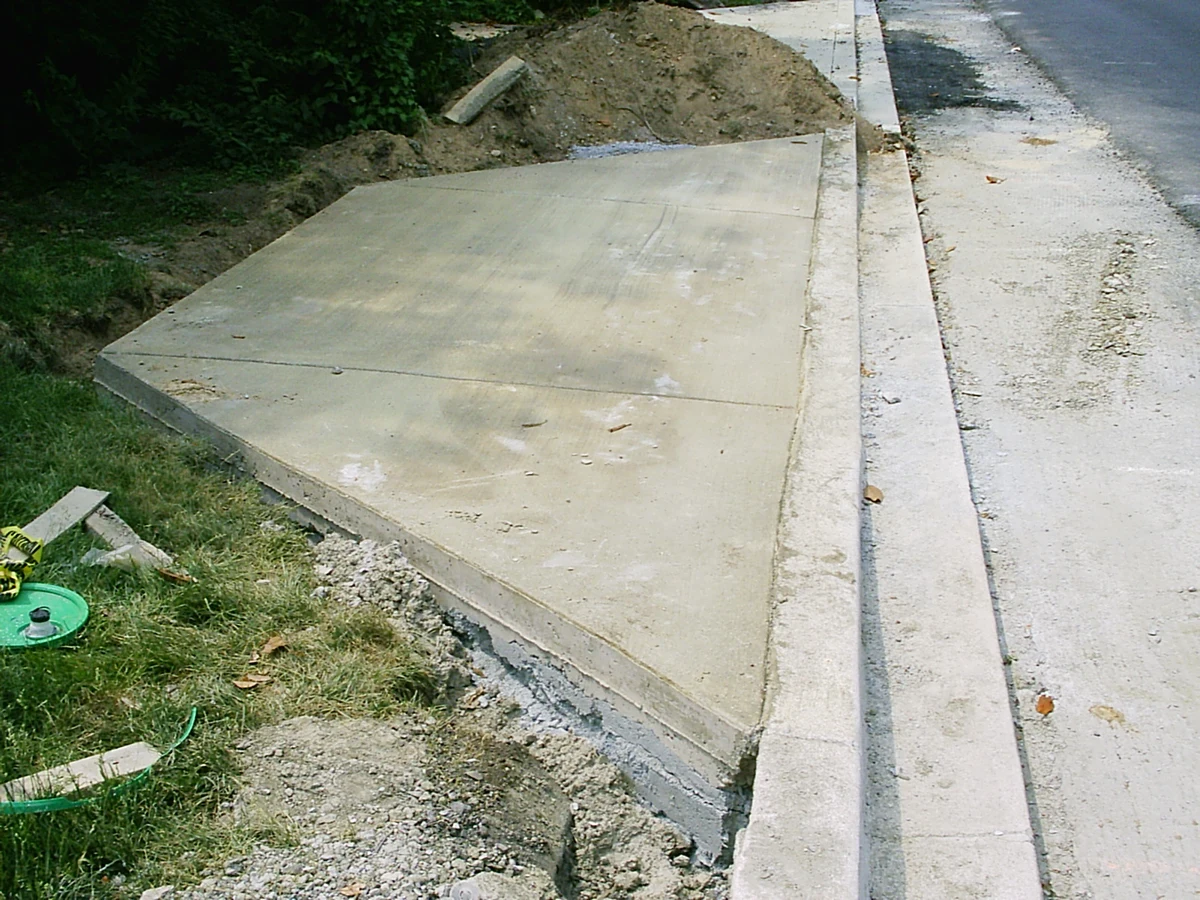 Concrete driveway apron meeting a sloped curb beside a street.