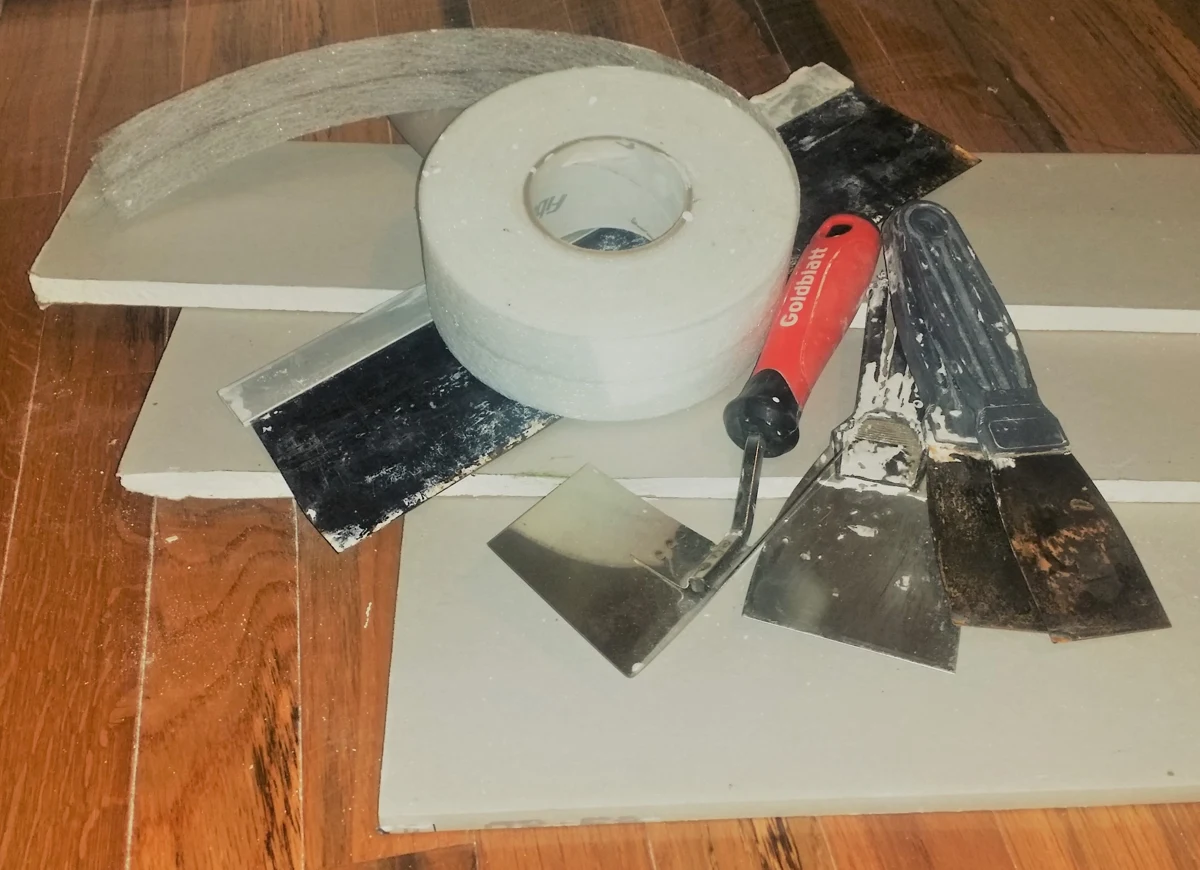 Drywall offcuts, joint tape and finishing knives laid on a floor.
