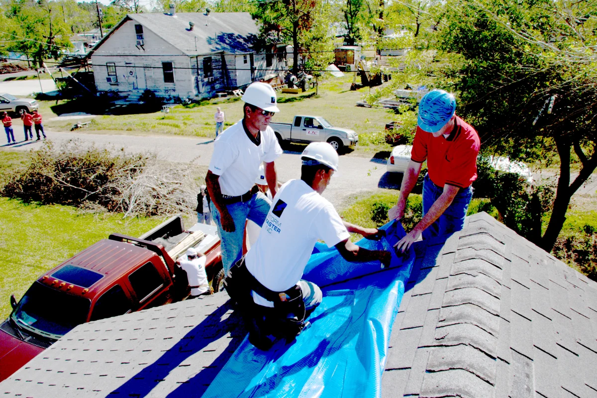 Crew fastening blue temporary covering to a damaged roof in Texas.