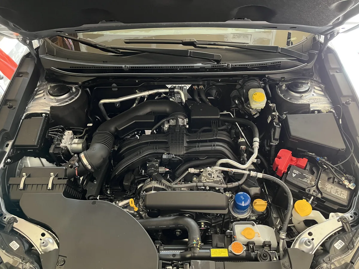 The engine bay of a 2023 Subaru Outback, with the engine in the middle and yellow and blue caps on the fluid fillers around it