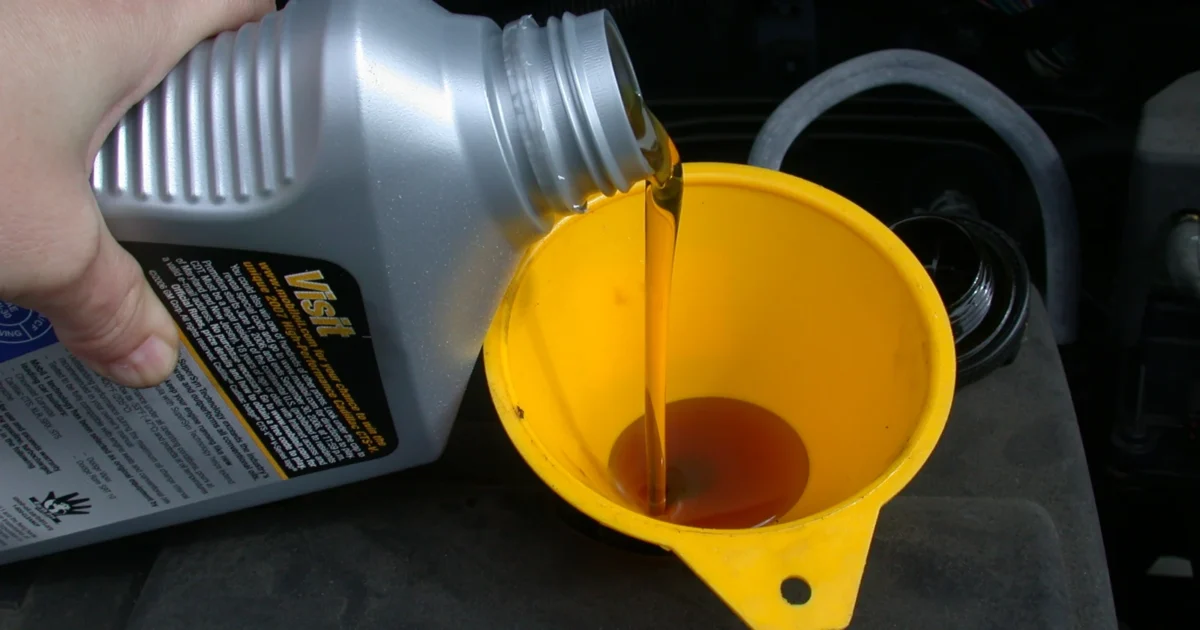 Oil being poured from a bottle through a yellow funnel into a car engine.