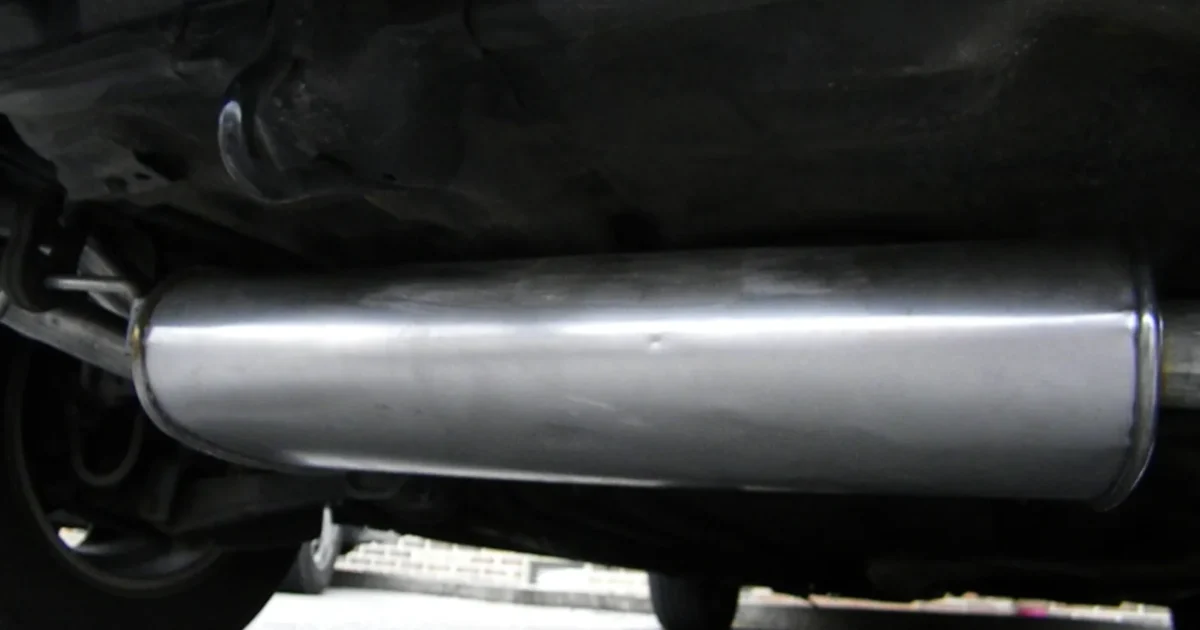 A shiny new muffler fitted under a small car, seen from the side at ground level